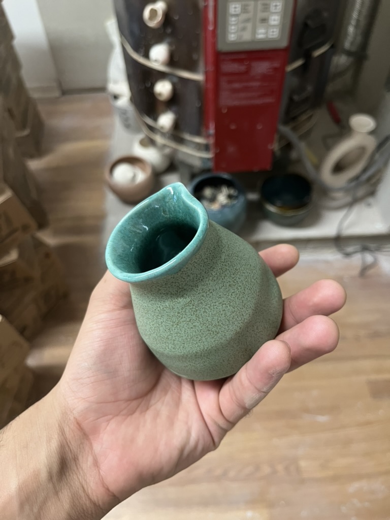 Hand holding a small green ceramic vase